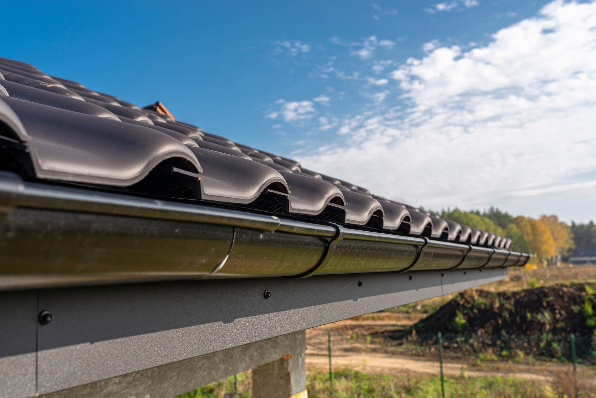 A metal, black gutter on a roof covered with ceramic tiles. Close up shot.