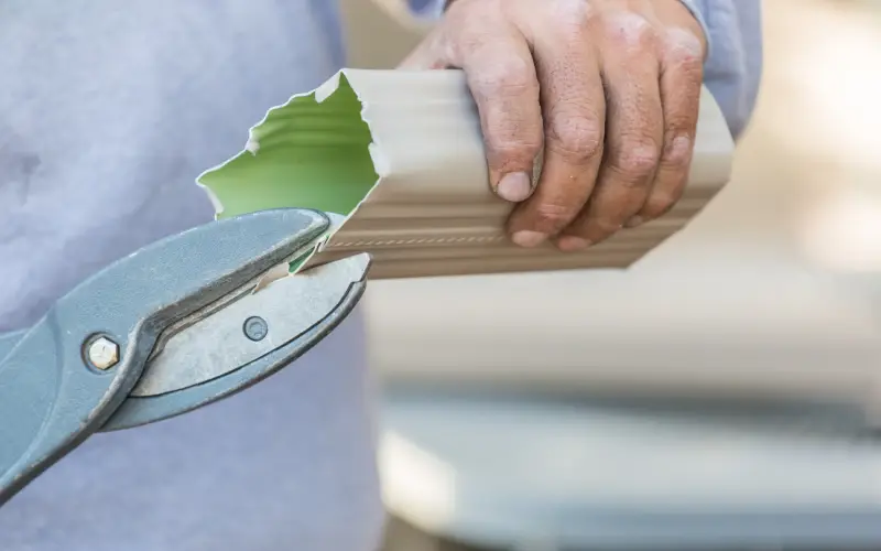 Close-up of a worker cutting a gutter section with metal snips during professional gutter cleaning in Federal Way.