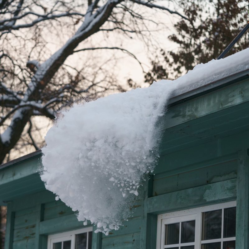 Ice dam prevention. Man holding shovel cleaning roof from snow, ice and icicles during wintertime Ice dam prevention. Man holding shovel cleaning roof from snow, ice and icicles during wintertime